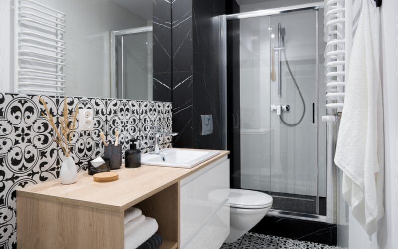 Small bathroom shower ideas featuring decorative ceramic wall tile with a floating vanity and dark black tiles on the shower surround