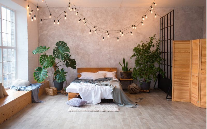 Pink-grey bedroom with hanging string lights on the ceiling and a wood plank and metal square room divider on the side