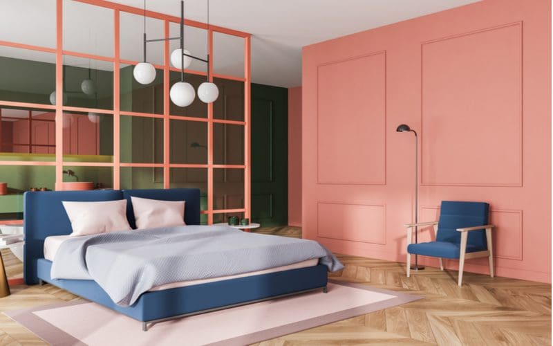 Pink wainscoted wall with unique square patterns line the bedroom covered in herringbone wooden flooring for a piece on grey bedroom ideas