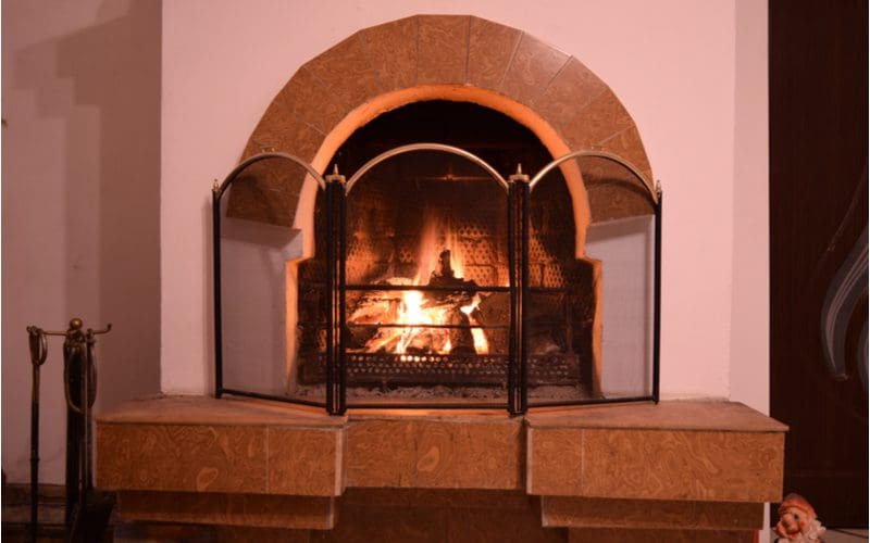 As an example of a fireplace tile idea, a wooden mantle frames a wood burning fireplace below a stucco chimney