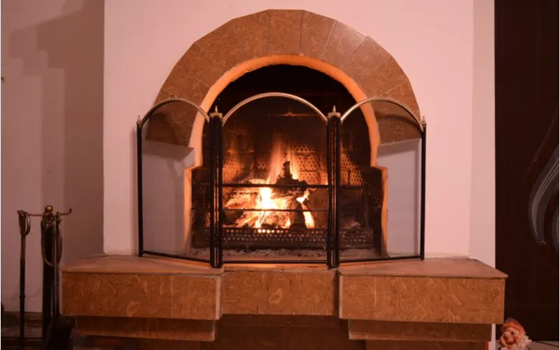 As an example of a fireplace tile idea, a wooden mantle frames a wood burning fireplace below a stucco chimney