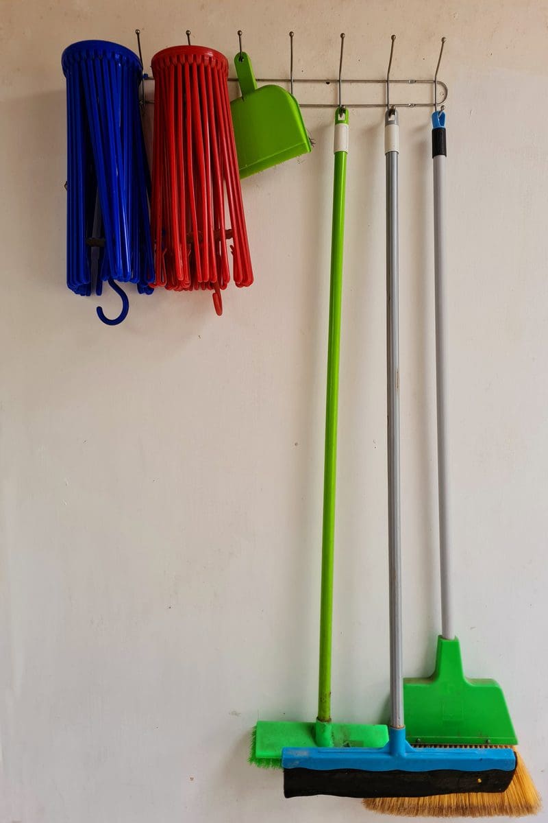 Small bathroom storage idea to hang brooms and mops behind a door from metal hooks