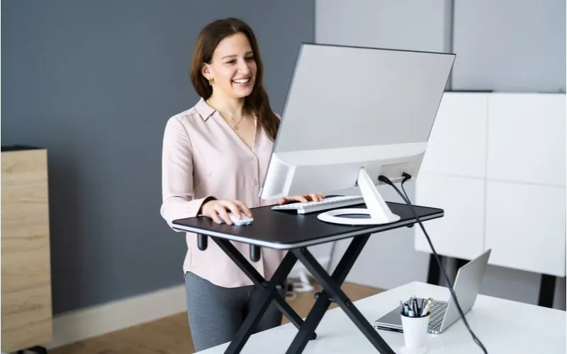 Image for a piece on desk dimensions showing a woman in yoga pants standing and working at a mobile standing desk station