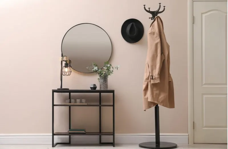 Idea for entry table decor featuring a simple metal coffee table below a round mirror next to a tall black metal coat rack