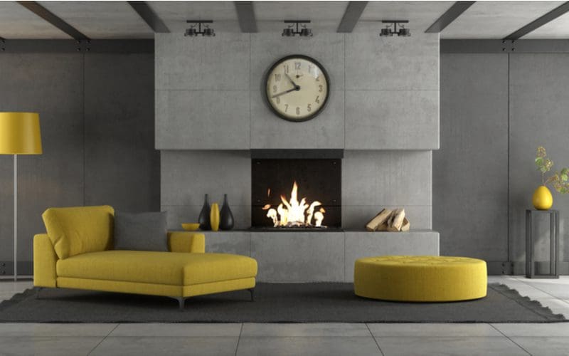 Image for an idea of fireplace tile with a concrete wall surrounding a big gas fireplace in a drab grey room brightened up with a yellow chaise lounger with a round ottoman