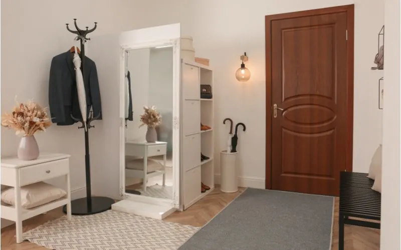 Entryway with a rustic wooden door and an entryway shoe storage cubby that's tall and skinny with doors on the left side alongside a floor mirror and a coat rack