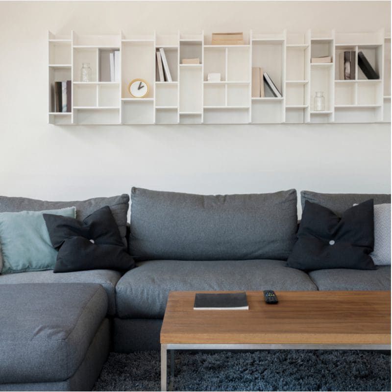 Geometric white wooden shelves above a grey couch with a tan table