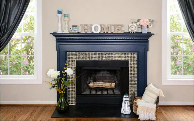 As an idea for fireplace tile inspiration, a small section of mosaic tile frames a wood fireplace with a dark blue mantle against a light beige wall
