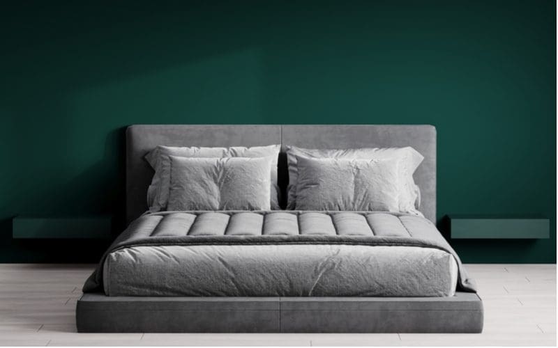 Green-teal accent wall with a grey bed with grey bedding