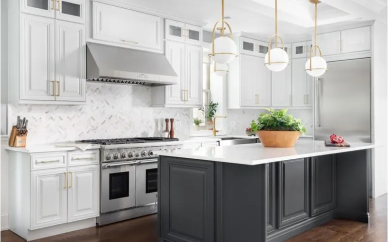 Grey angled farmhouse backsplash idea in a modern farmhouse-style kitchen with grey accent cabinets and white main cabinets with gold hardware and white granite counters