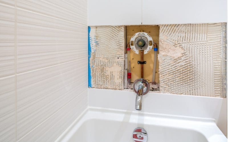 For a piece on the parts of a shower, a cutout of a shower pipe and valve being fixed by a repairman