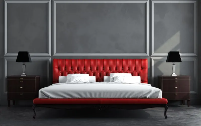 A red tufted bed with white linens sits in front of a grey paneled wall