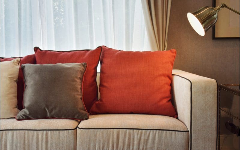 Image for a post on what color pillow for a brown couch featuring a light brown couch with dark brown, tan, and red pillows as accents