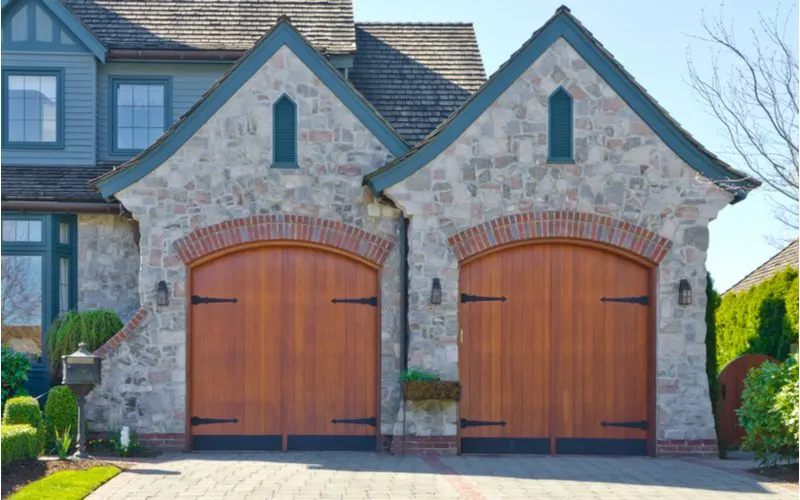 Medieval brick home with two brown garage doors pictured with a big porch overhang