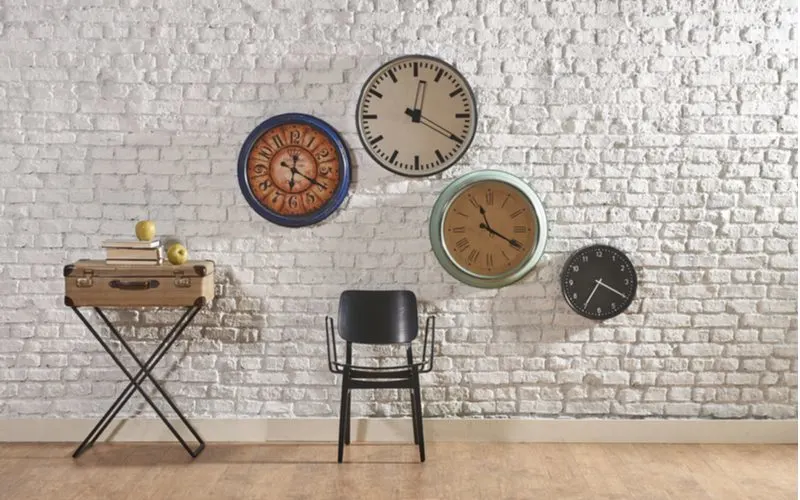 Wall clocks hang on a white painted brick wall for ideas on how to cover walls cheaply