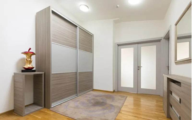 Sliding wood closet door idea with metal trim and accents in the middle in a room with pine hardwood floors in light brown color, white walls, and grey trim and furniture