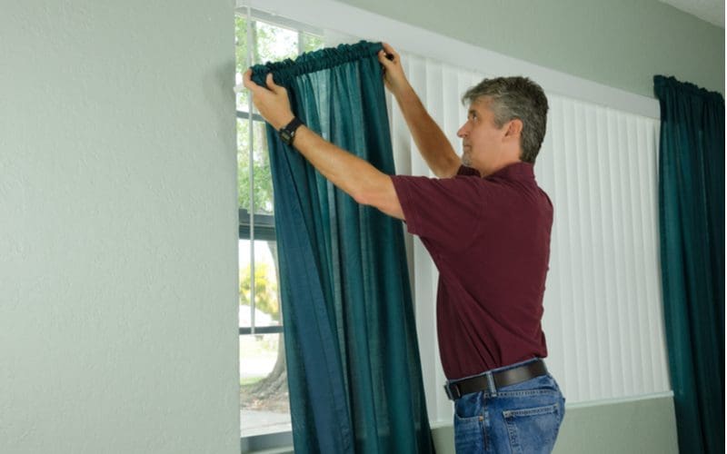 Guy hanging curtains in a gray painted living room for a piece on what color curtains with gray walls