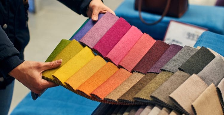 Featured image for a piece on the best fabric for dining room chairs featuring a number of textile samples laid out in various colors being held at the end by a man
