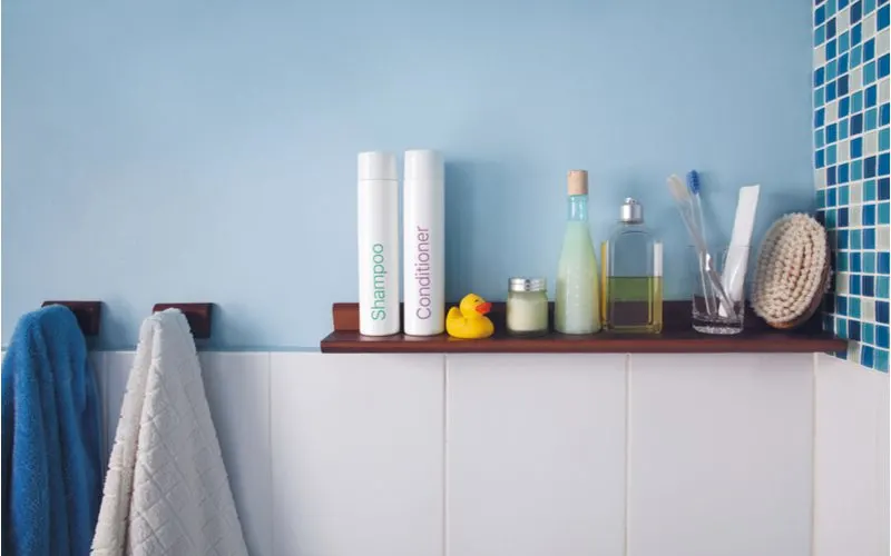 Hygiene shelf mounted just above the tile on a blue wall for a piece on bathroom shelf ideas