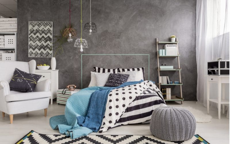 Grey bedroom idea with a black and white striped and polka dot comforter, a dark grey wall, and a painted white floor