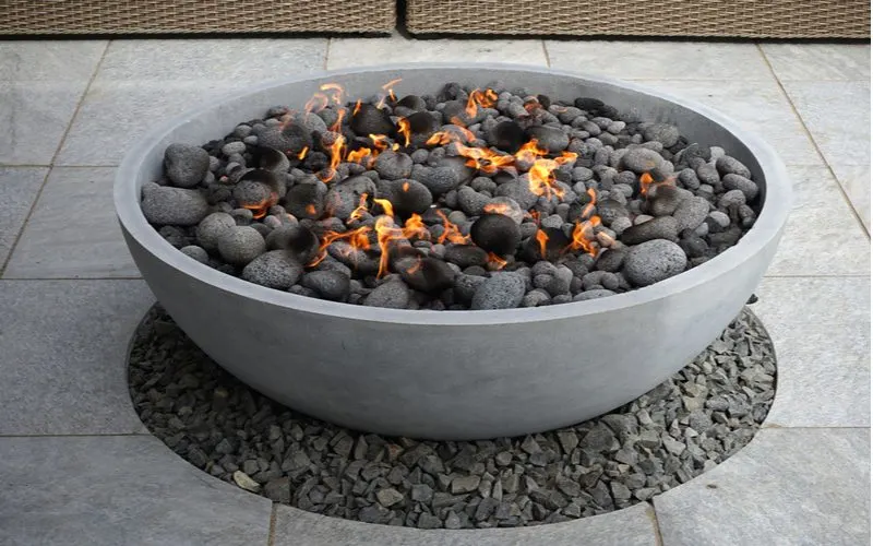 Modern stone bowl gas firepit with rock trim nit he middle of a stamped concrete patio