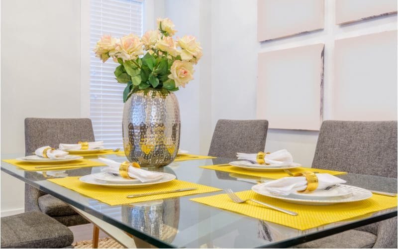 Dining room table centerpiece idea featuring flowers in a silver vase with yellow placemats that bring a bit of color into the room