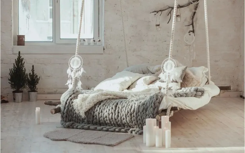 Image of a suspended bed with a big knit blanket resting on the mattress in a brick walled room for a piece on grey bedroom ideas