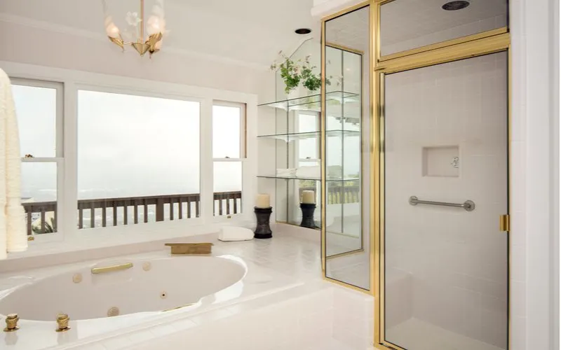 White and gold bathroom idea with a gold-trimmed shower door, gold tub fixtures, and white walls with a view through big picture windows that overlooks an ocean