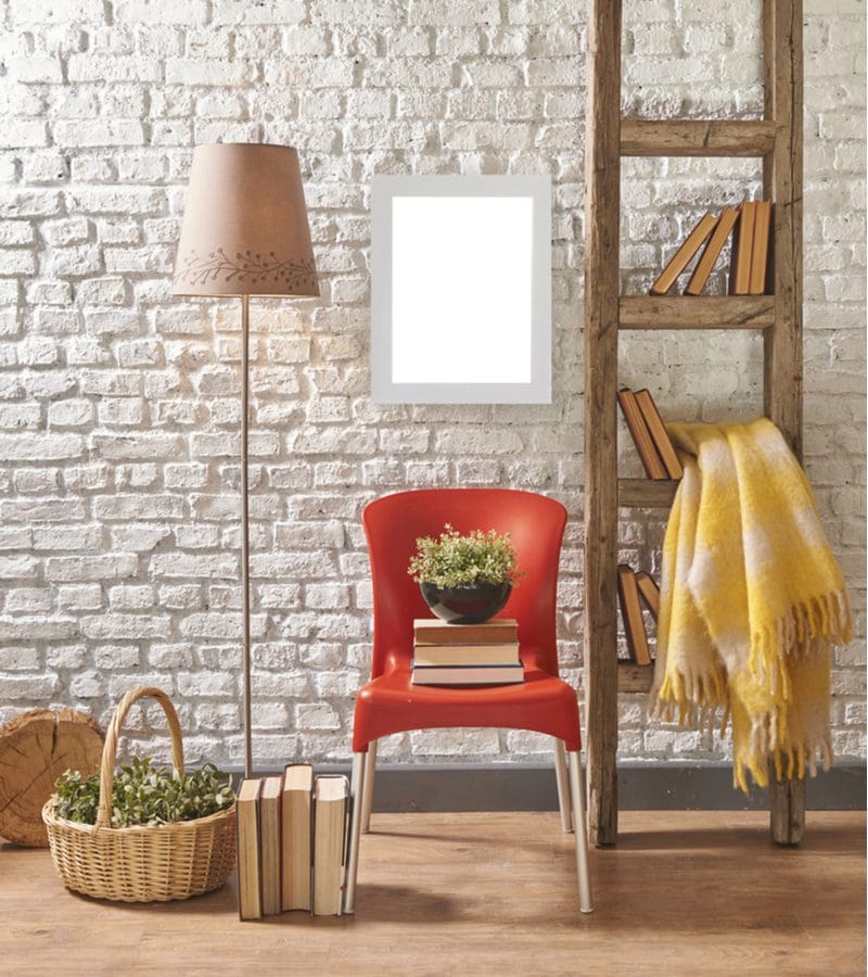 Men's bedroom idea with a ladder shelf in natural wood color next to a red chair by which sit books