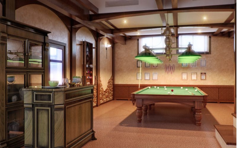 For a piece on man cave ideas, a room with a pool table and wooden wall paneling sits in a dimly lit basement