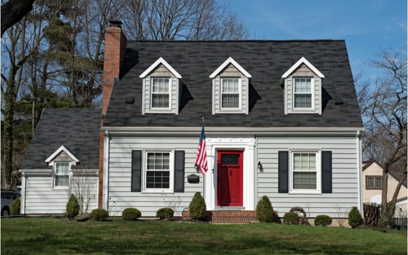 Front door color for gray house idea featuring a red door on a gray cape cod style home sitting on a well manicured lawn