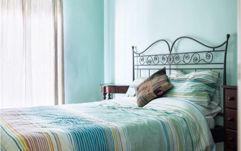 Bedroom idea with bright painted teal walls and a dark skinny metal bedframe with blue and red and white bedding