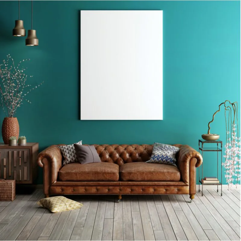 To help answer what color walls go with brown furniture, a nature-inspired living room with green wall, light grey flooring, and a plain white picture above the couch