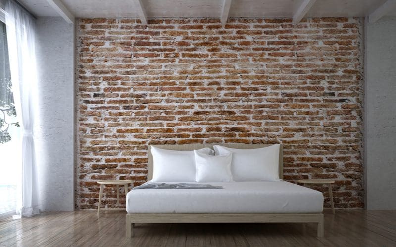 Photo of a bedroom with a red brick accent wall between two grey walls 