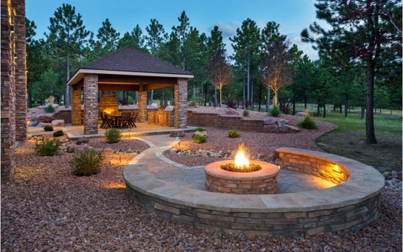 Image for a piece on fire pit ideas featuring a giant paver patio with a walkway to a block retaining wall bench around a fire pit