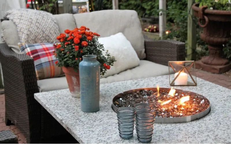 For a roundup on fire pit ideas, a granite table with a metal fire pit in the middle surrounded by wicker cushioned chairs
