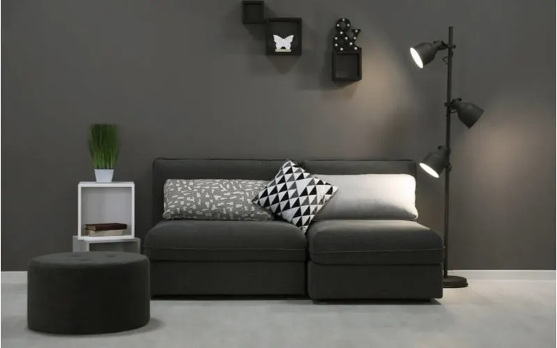 For a grey flooring living room idea, an elegant dark grey couch with a dark grey wall and black lamps and accents sits on a light grey living room carpet