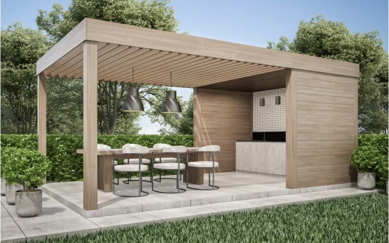For a roundup of cool pergola ideas, a wooden bar with three walls and a partial roof that turns into a pergola above a stamped concrete patio