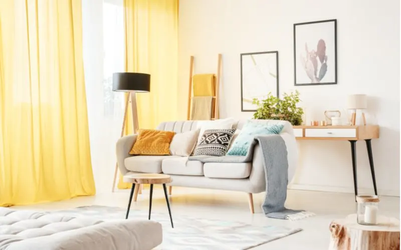 To illustrate when curtains should touch the floor, a modern living room with yellow curtains and beige furniture with off-white walls is pictured
