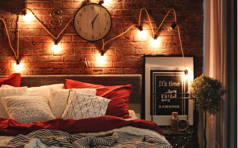 Mens bedroom idea featuring edison bulbs hanging from nails on an exposed brick wall above the headboard