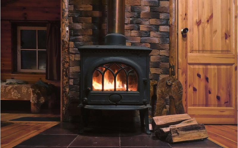 Fireplace tile idea that uses brick behind the black wood burning chimney pipe in a rustic-looking cabin