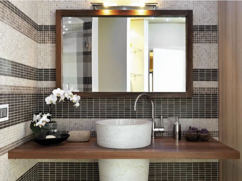 For a piece on small bathroom ideas with shower, a modern resort-style bathroom with glass mosaic tile lining the wall with a shower and closet visible in the large mirror