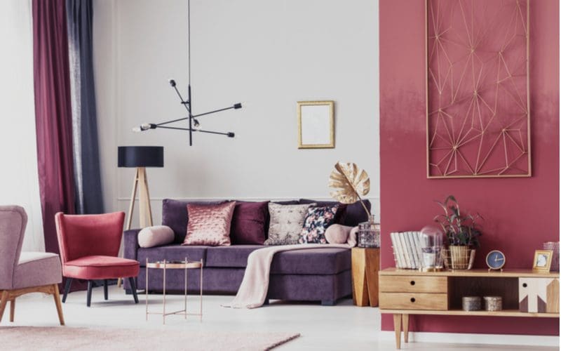 Colorful modern cozy living room idea with a red wall accenting an otherwise drab grey room with a blue acouch and boho-style coffee end table