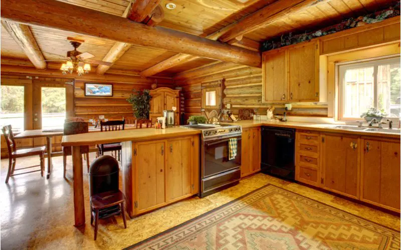 Country inspired kitchen with log timber frames and a log cabin-style wall covering with rustic cabinets made of natural pine wood