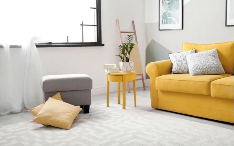 Modern cozy living room with a yellow couch, grey ottoman, and white walls with black window trim
