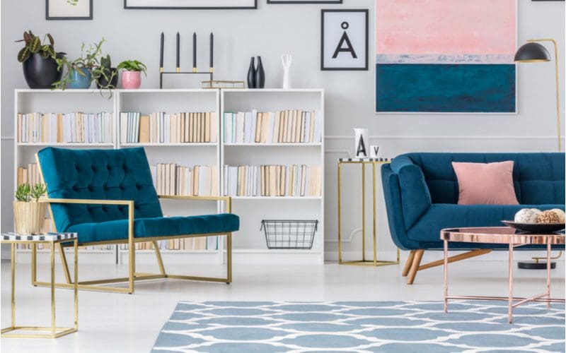 Navy blue suede armchair and loveseat in a modern cozy living room with a bookshelf and ample framed prints in navy colors