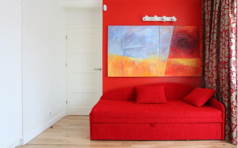 Teen boys' room decorating idea with a red wall and a red pull-out futon bed below a large abstract painting