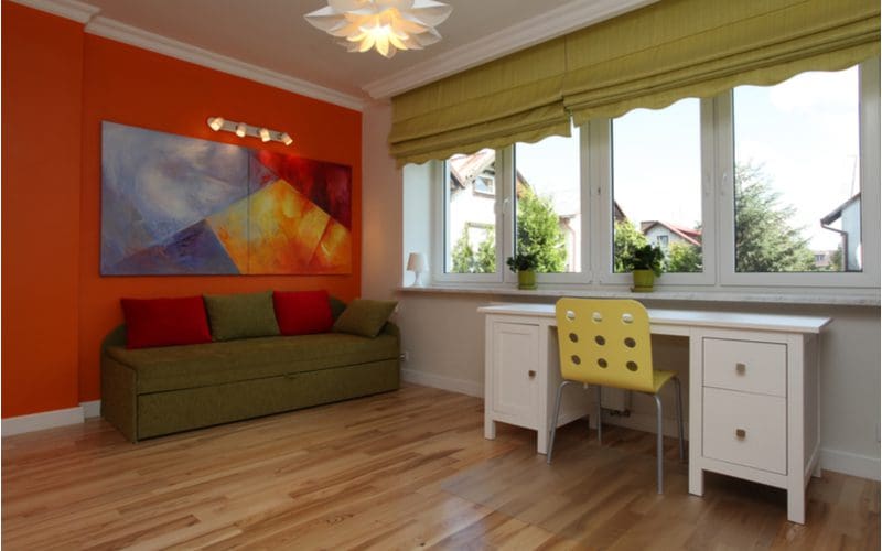 Colorful and Contemporary teen boys room decorating idea using a red wall, a large two-panel canvas painting, and wood floors with a simple white desk with a yellow chair