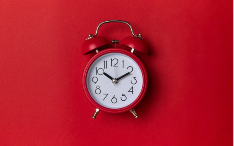 Red analog alarm clock is pictured on a red background for a piece on types of clocks