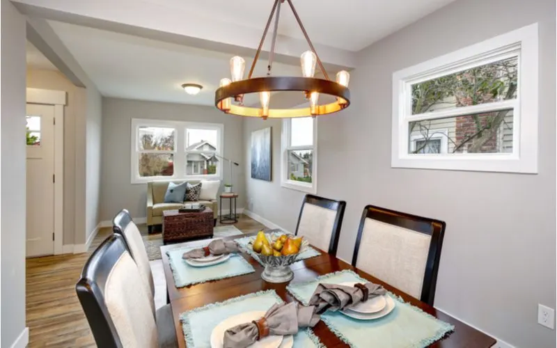 Dining room decorated in a transitional style home featuring a rustic-industrial style round light fixture with edison bulbs and simple grey walls with dark wood floors